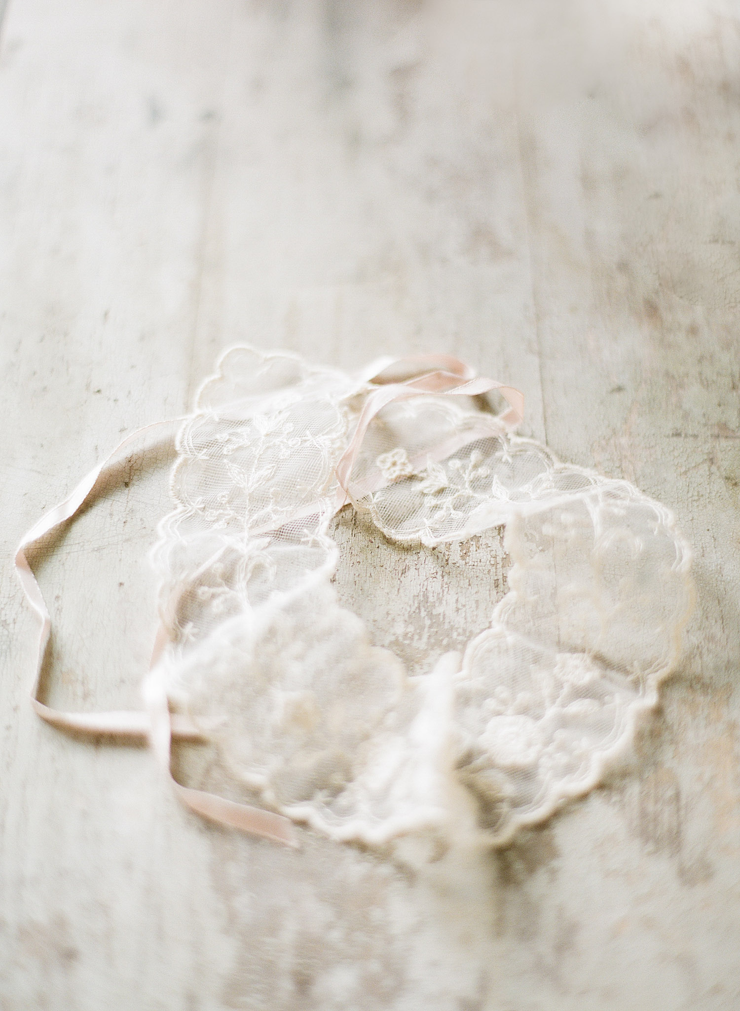a vintage lace garter lays on a distressed wood table while destination wedding photographer Lexia Frank photographs this wedding on film at the Northwind Perennial Gardens in wisconsin