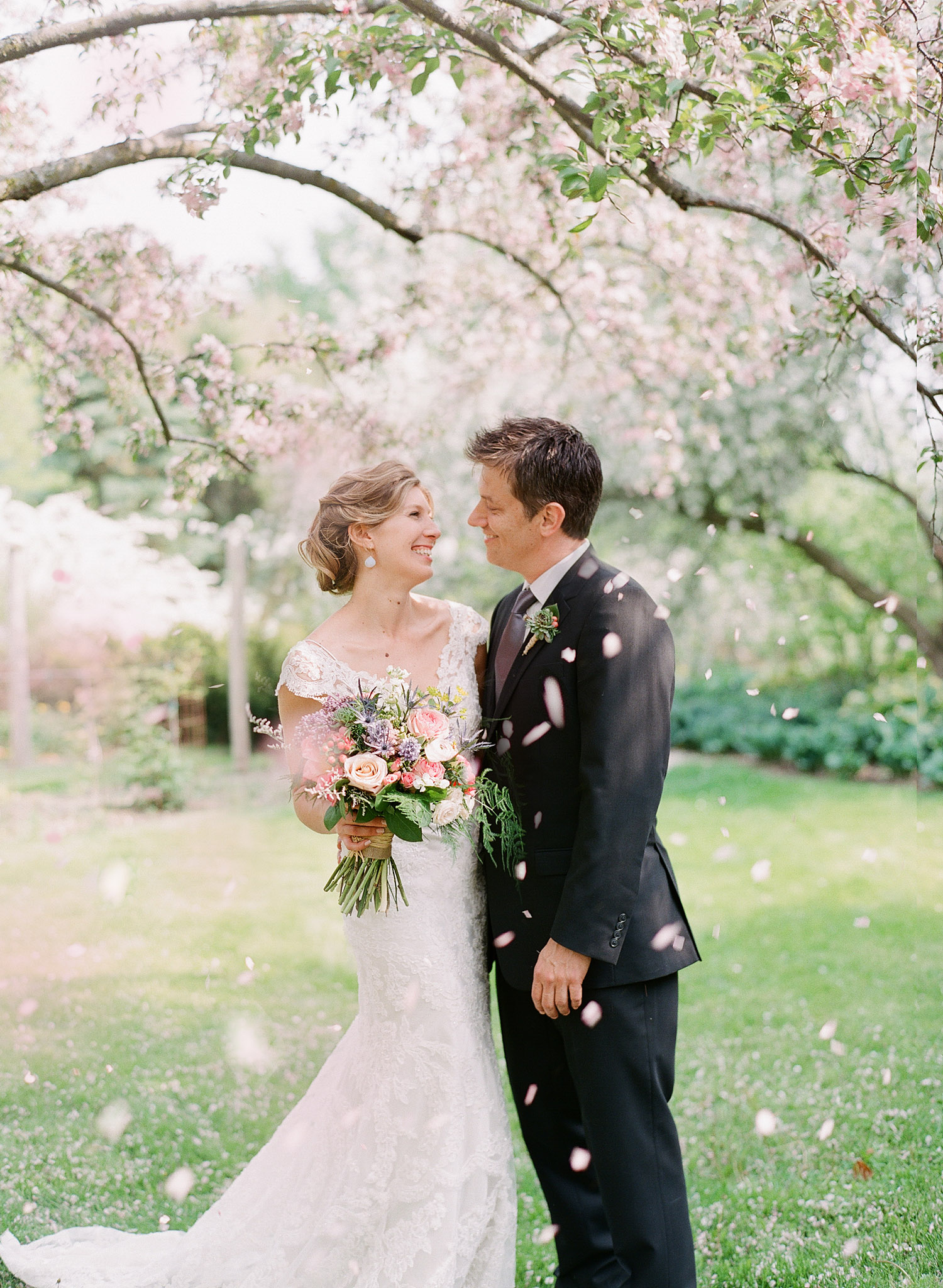 bride and groom have their first look under falling petals at their wedding at Northwind Perennial Gardens in wisconsin while destination photographer Lexia Frank photographs on film