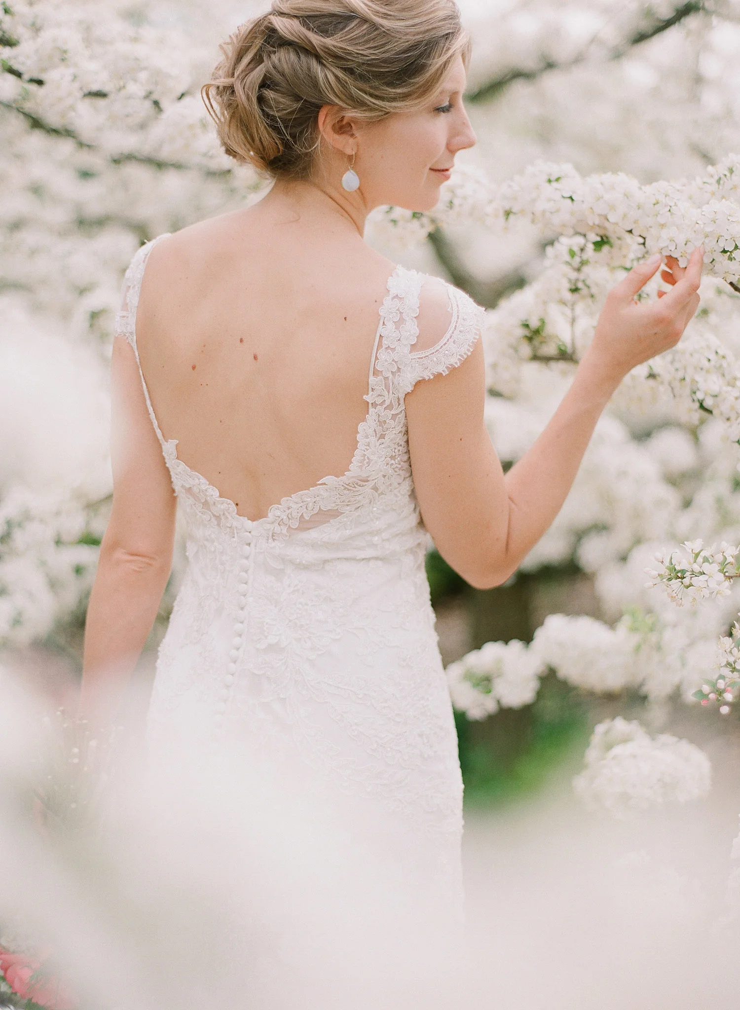 bride wears lace wedding dress with cap sleeves and smells the springtime blooms at her springtime wedding at Northwind Perennial Gardens in wisconsin while Destination wedding photographer Lexia Frank photographs her wedding on film 