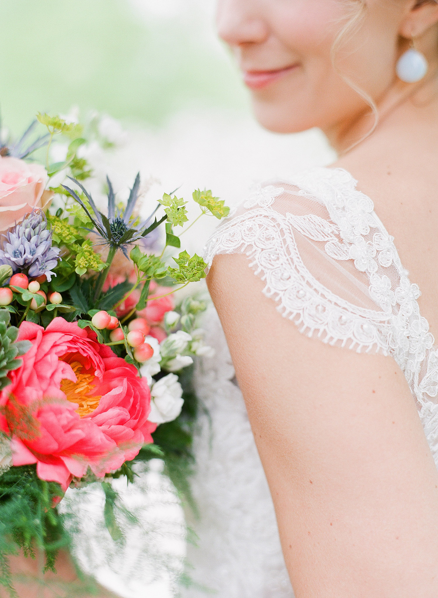 bride wears a vintage lace dress with cap sleeves and holds her asymmetrical bouquet of peonies ranunculus and ferns at her springtime wedding at Northwind Perennial Gardens- a beautiful Wisconsin Wedding venue- while Destination Wedding Photographer Lexia Frank photographs her wedding on film 
