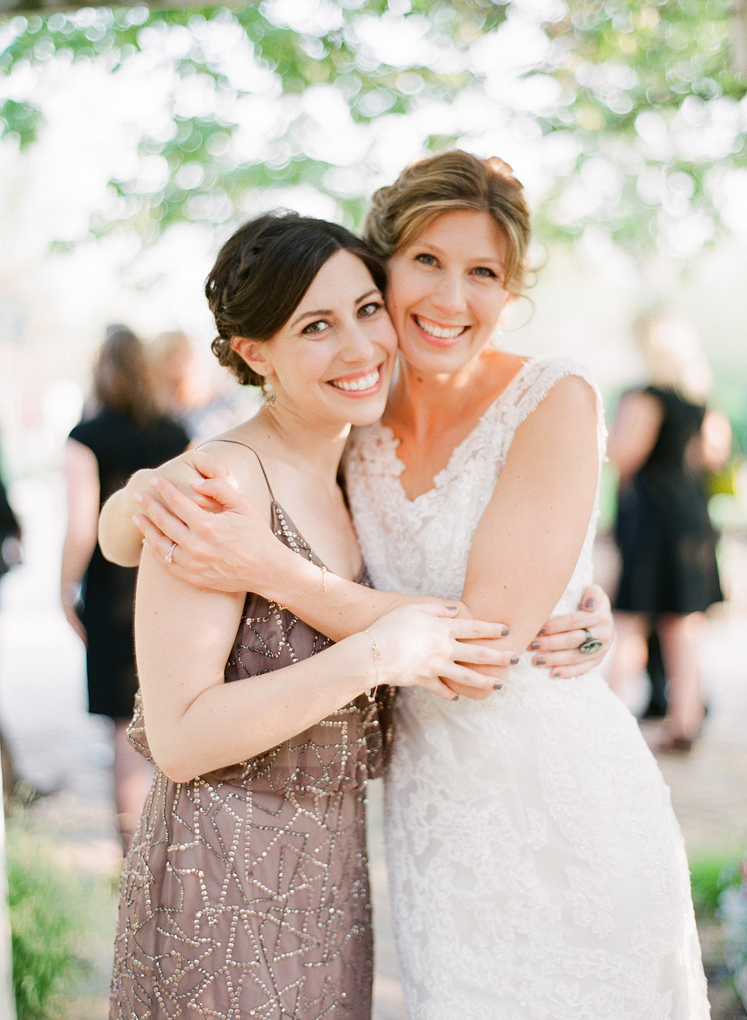 bride hugs bridesmaid at this springtime wedding at Northwind Perennial Garden - a beautiful wisconsin wedding venue - while Destination wedding photographer Lexia Frank Photographs this wedding on film