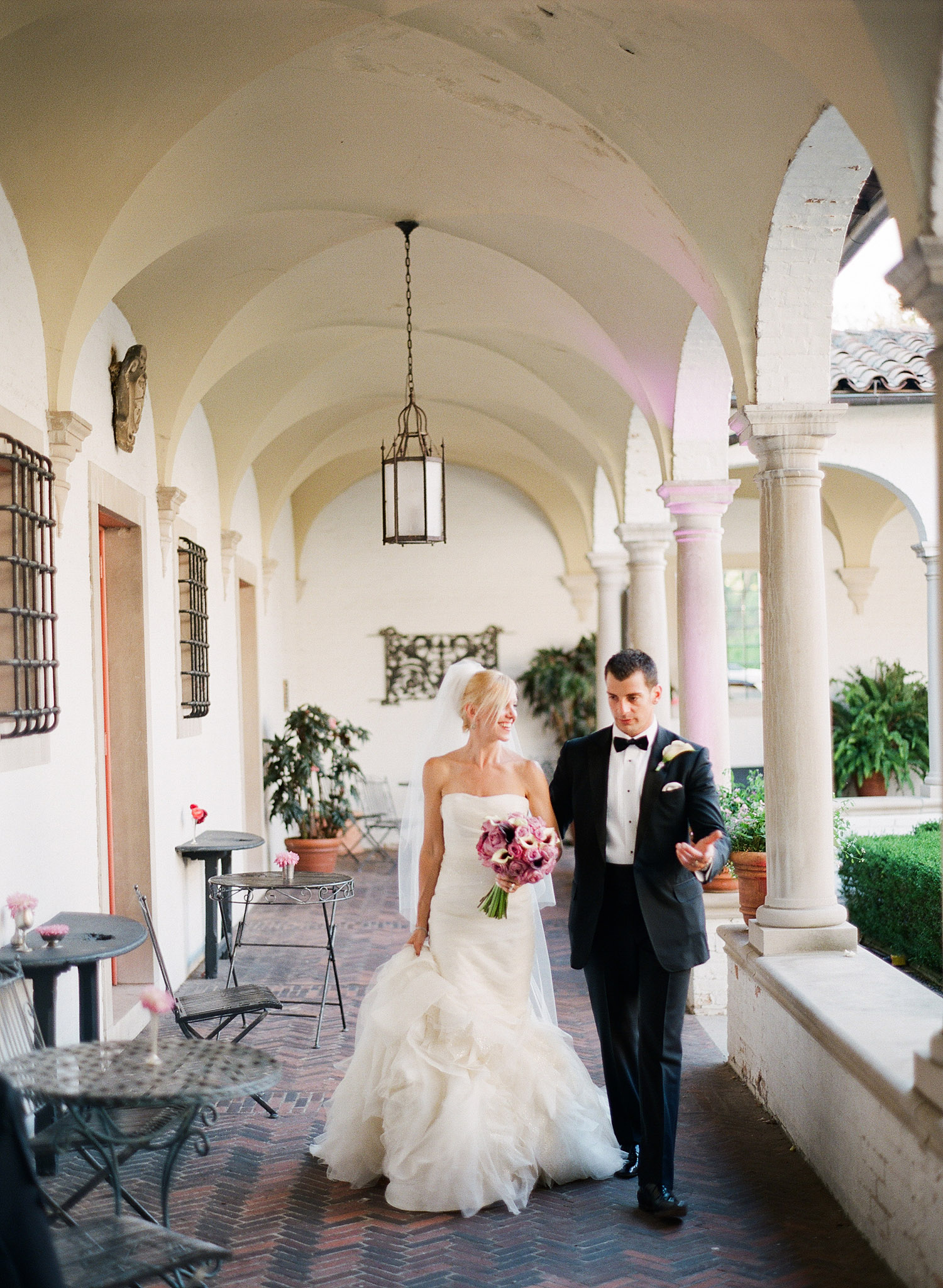 groom leads a bride through the columned corridors of the italian villa at their destination italian wedding while Destination wedding photographer lexia frank photographs their wedding on film at the Villa Terrace