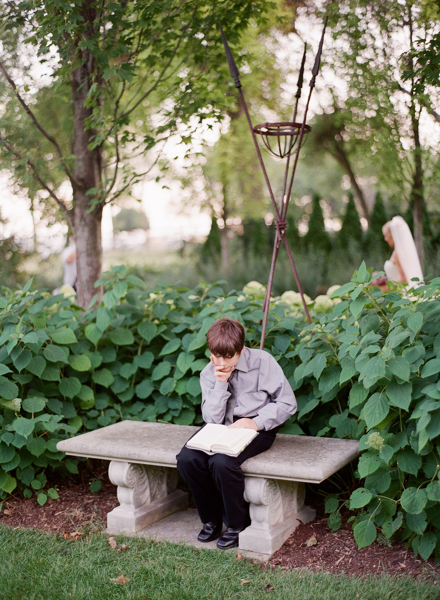 boy reads during the cocktail hour at the italian wedding at the Villa Terrace while Destination wedding photographer lexia frank photographs the weddng on film