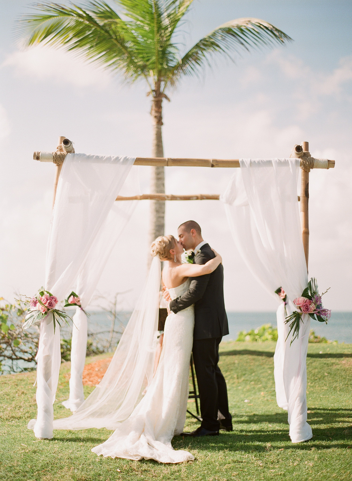 bride and groom kiss under their bamboo chuppa at their Vieques Island Wedding at the W hotel while Destination wedding photographer Lexia Frank photographs their wedding on film 