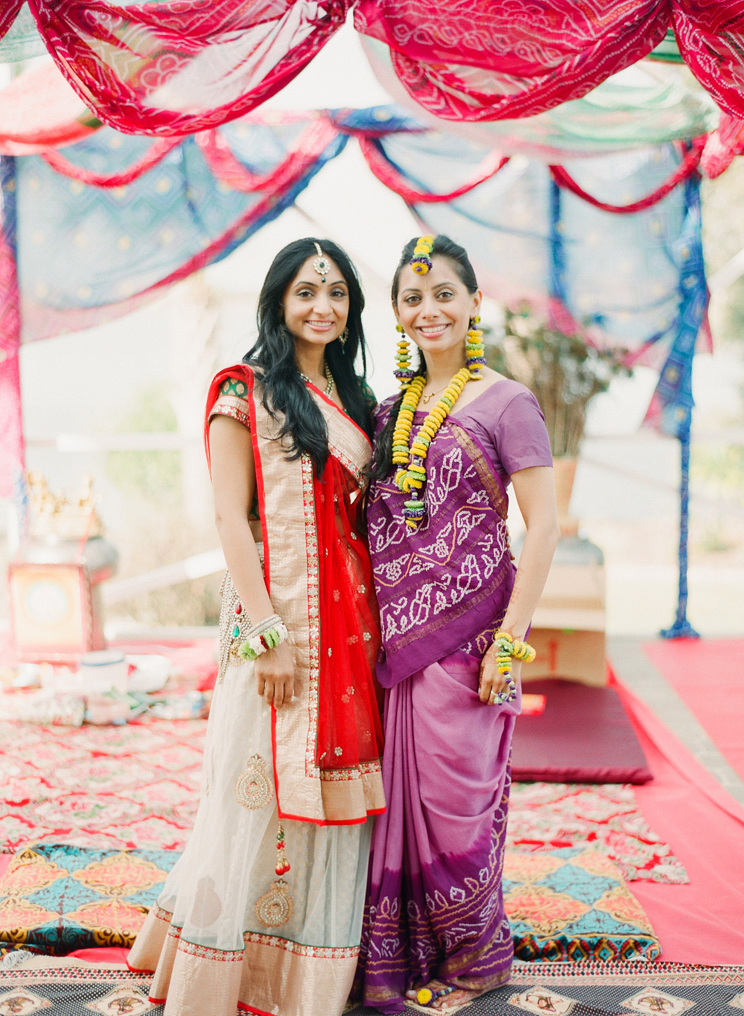 bride and her sister pose for a photograph while bride wears a purple sari and floral jewelry and a floral tikka headpiece and floral ankle jewlery and bracelets for her hindu wedding in palm coast florida at the hammock beach resort while Destination Wedding Photographer Lexia Frank - a top indian wedding photographer - photographs this luxury indian wedding on film because she is a film photographer who shoots weddings in florida and worldwide 