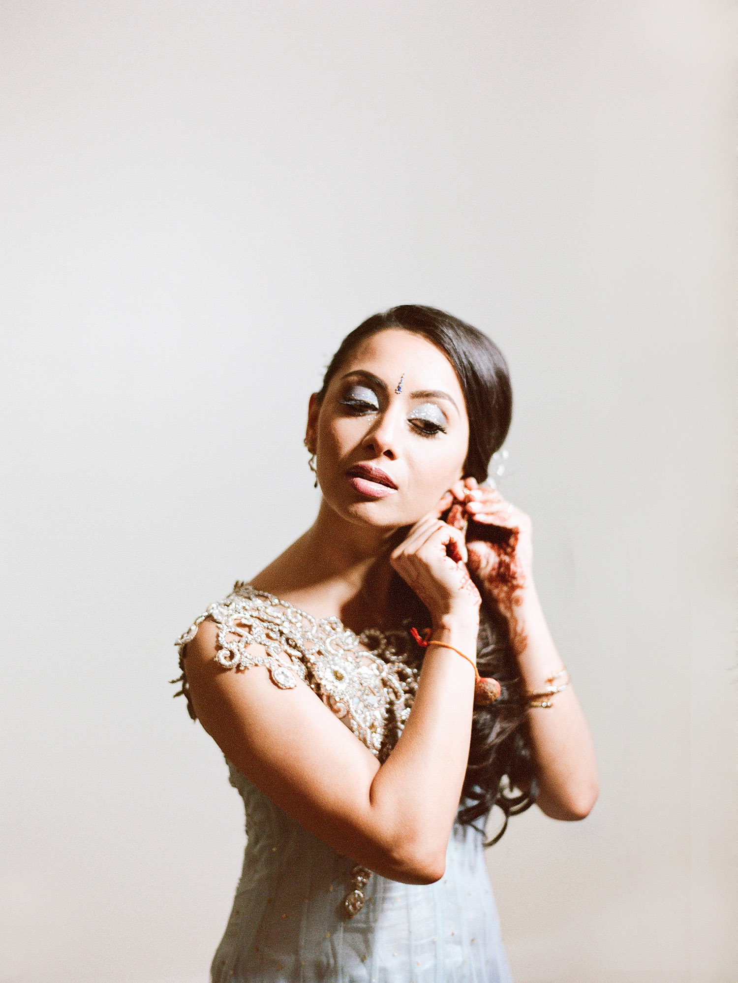 indian bride gets ready for her hindu wedding and chooses a light blue lengha for her rehearsal dinner dress ideas and puts on her earring during her indian wedding in palm coast florida while Destination Wedding Photographer Lexia Frank - ranked top indian wedding photographers in the UW and India - photographs her luxury indian wedding on film because she is a film photographer who photographs luxury indian weddings on film in florida and worldwide for brides who love maharani weddings, south asian bride magazine and manish malhotra 