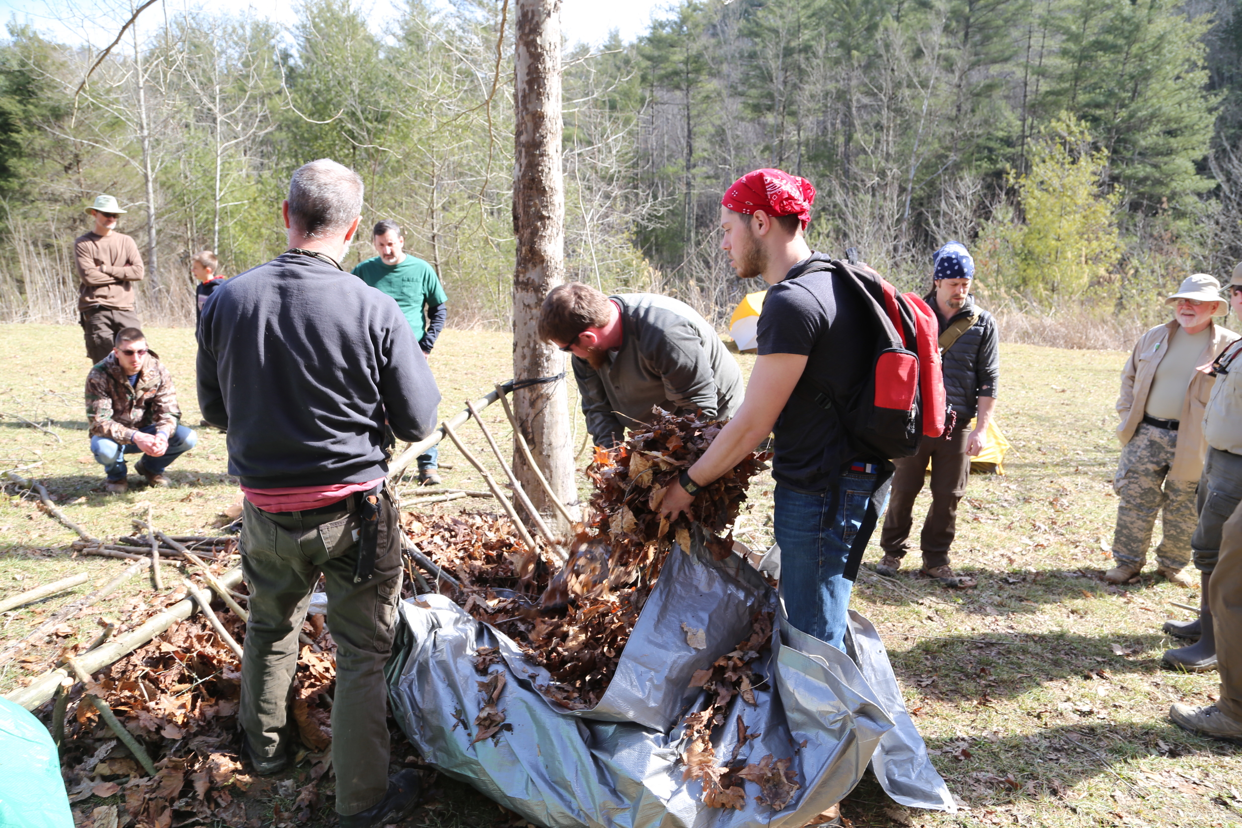 Course participants pile on leaves during the construction of a debris hut. Photo by Todd Nystrom.