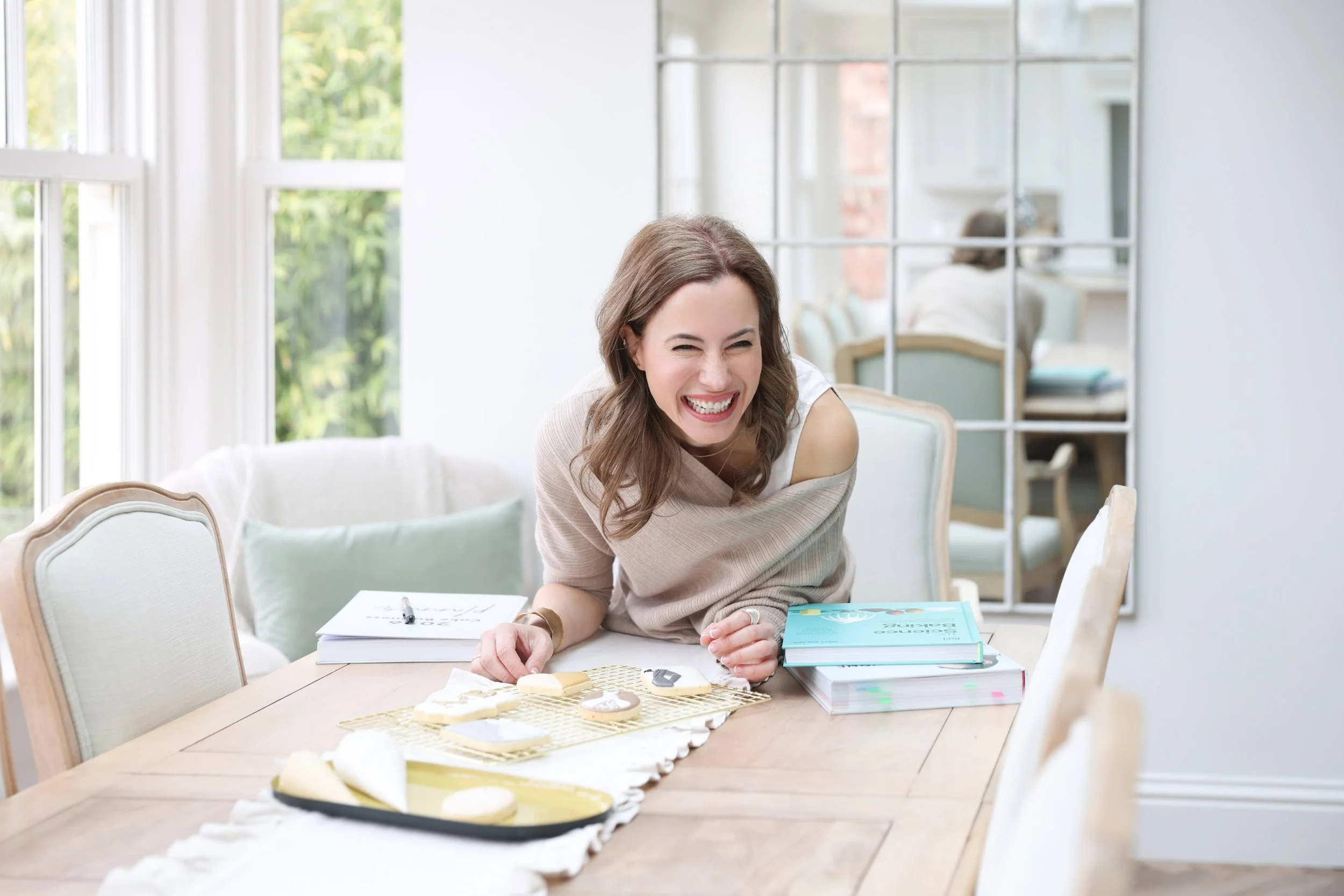 Katerina, owner of Floc Bakes, laughing portrait at a dining table with baked cookies