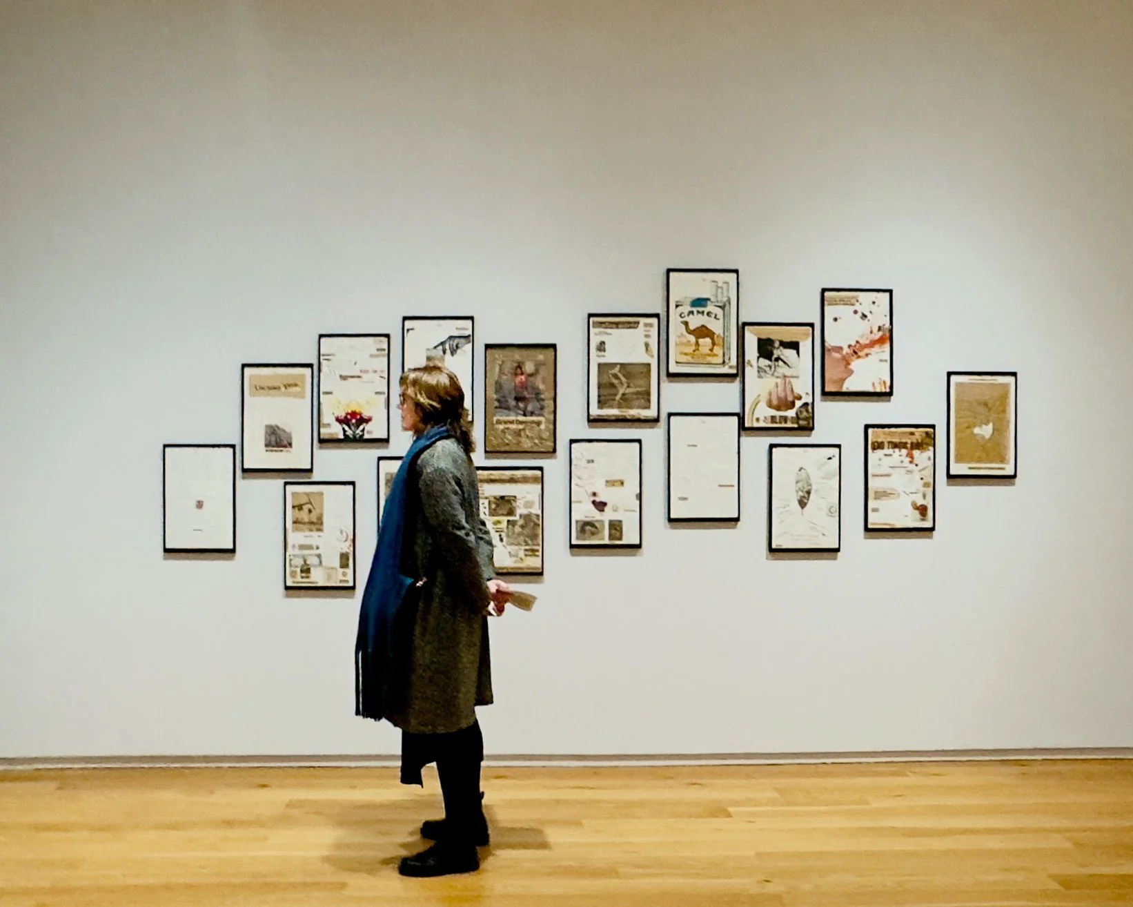 A woman standing and looking at framed artwork on a gallery wall, with a wooden floor.