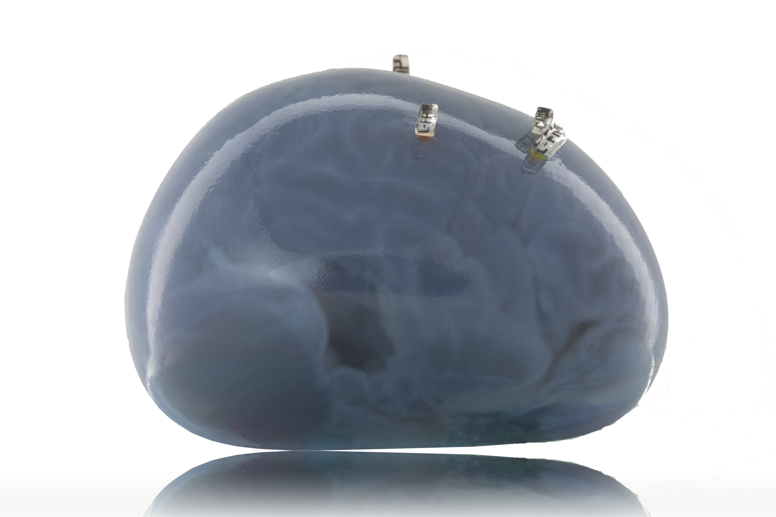 A polished, dark-colored, semi-precious stone with metal prongs attached for setting in jewelry, resting on a reflective surface