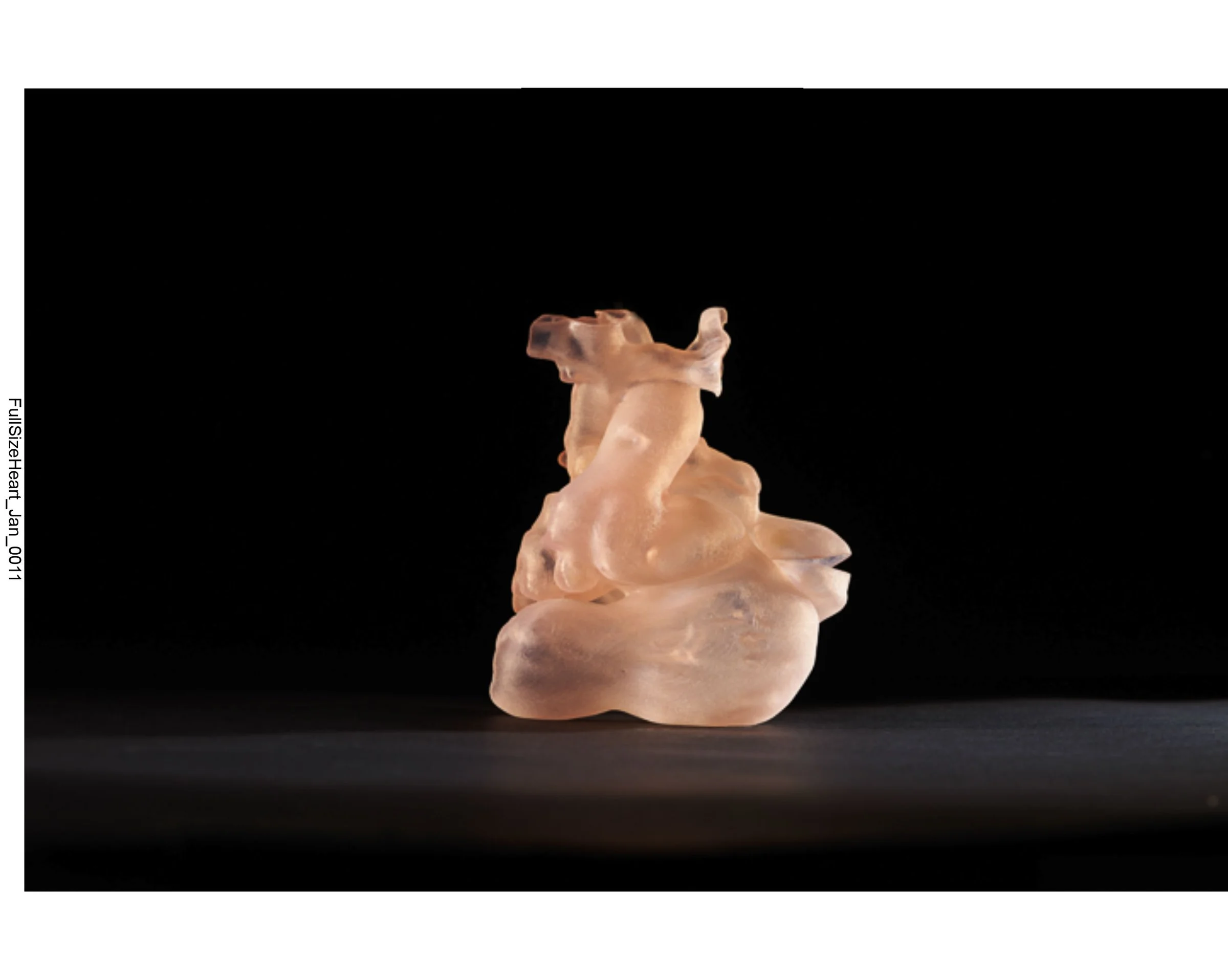 A small, abstract, peach-colored sculpture with smooth, flowing curves placed on a dark background.