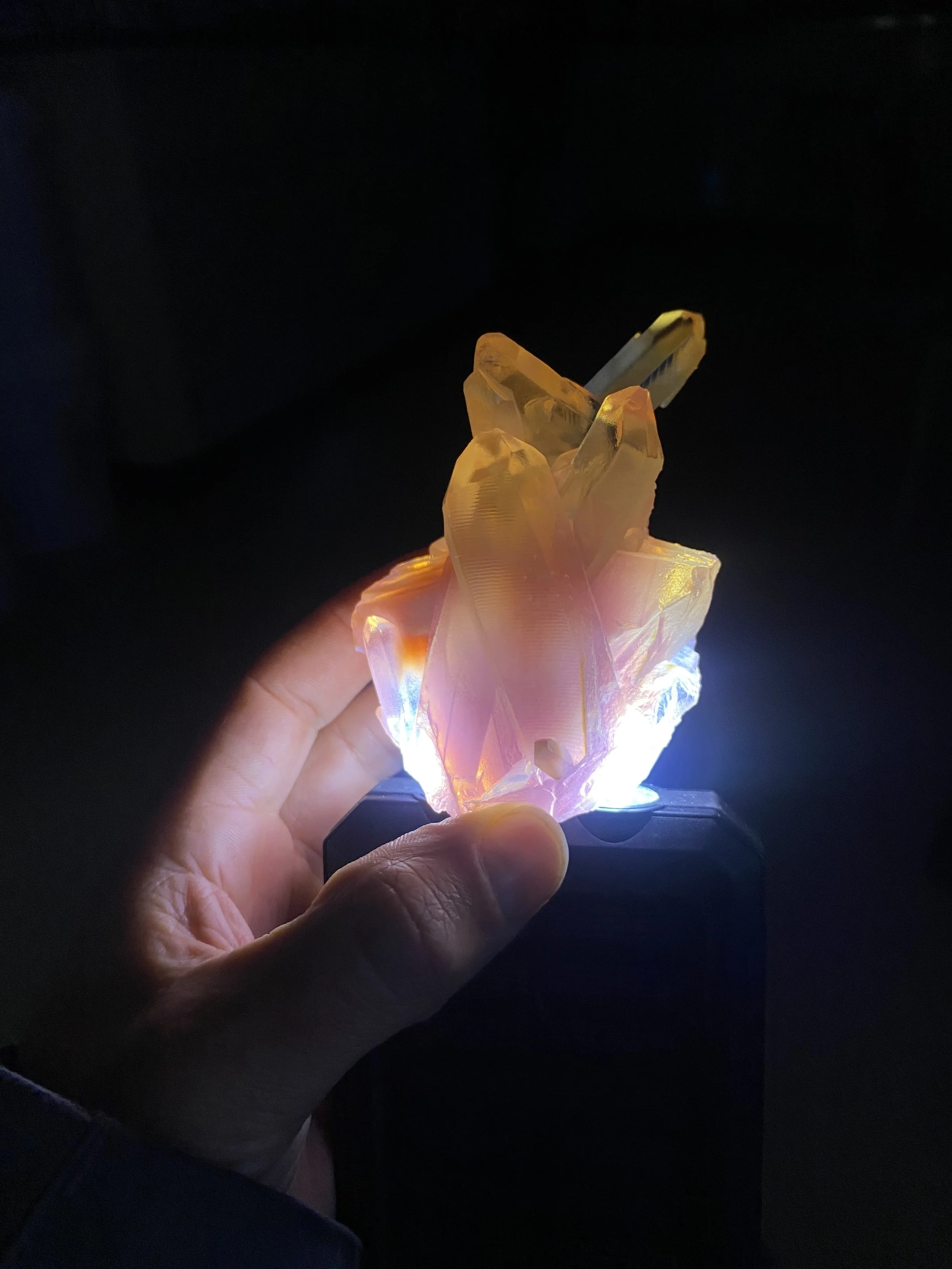 A hand holding a glowing, colorful, crystal-like sculpture against a dark background.