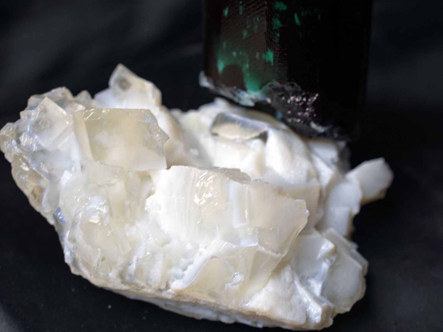 Close-up of a rough, crystalline white mineral or substance with a black and green container in the background.