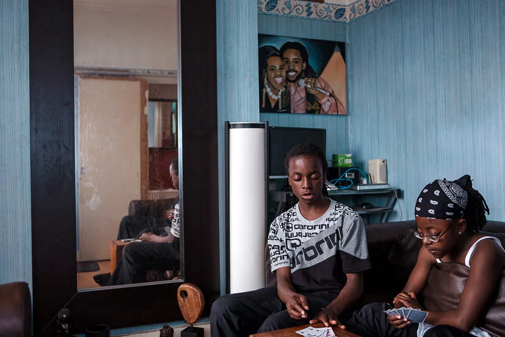 Joel and his sister playing cards in their front room, London Fields, 2008 From a family of 8 brothers and one sister, living on the edge of London Fields, Joel was geographically in the middle of one of the worst and most well-known turf wars in London – the London Fields Boys vs The Holly Street Boys. Although Joel was never in a gang, the violence affected his life daily. Here he was inside playing cards with his sister because they didn't feel safe to play outside, he had to take long routes around the suburb to cross it due to the risks of being seen in the neighbouring streets near Holly Street. 