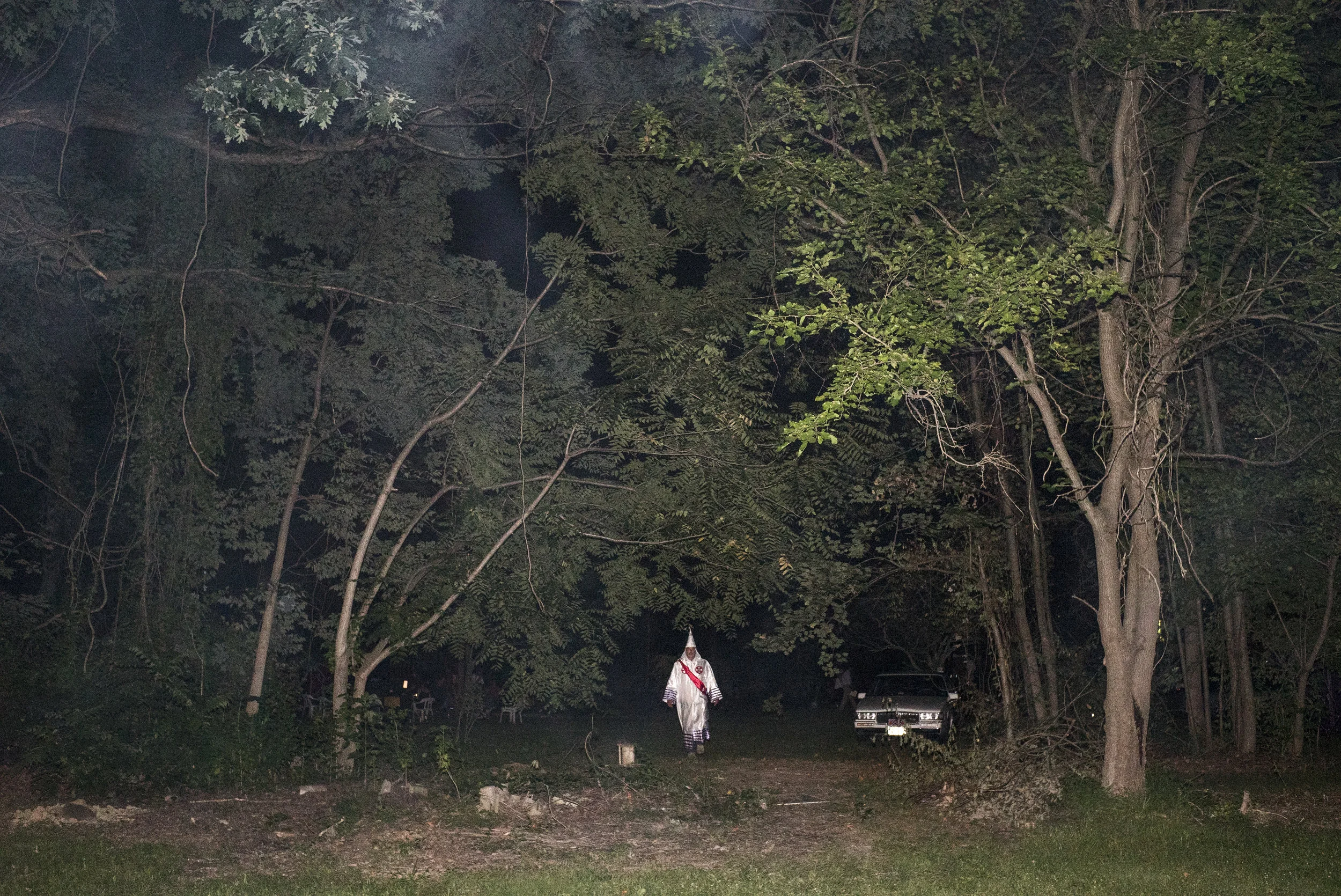 Maryland. 2015. The KKK had boasted that dozens from their Klan chapter would attend the rally and cross burning, but there were only a few people when we showed up, including a British TV crew and a freelance photographer. After a few vague excuses, the 6 or 7 Klan members changed into their robes and began a show amongst themselves. One of the leaders started his speech. He shouted that there were ISIS training camps being created by the United Nations with FEMA (Federal Emergency Management Agency) whose fighters would then take American’s guns away. This plan was allegedly hatched by Barack Obama (or Barry Soetoro as he was called by the Klan. Soetoro was the surname of Obama’s stepfather and that he was briefly called Barry Soetoro in elementary school in Indonesia has been used as evidence that Obama was not born in America). After finishing, the hoarse-voiced Klan member burned the UN flag and stomped on it, to the tepid cheers from the small crowd.