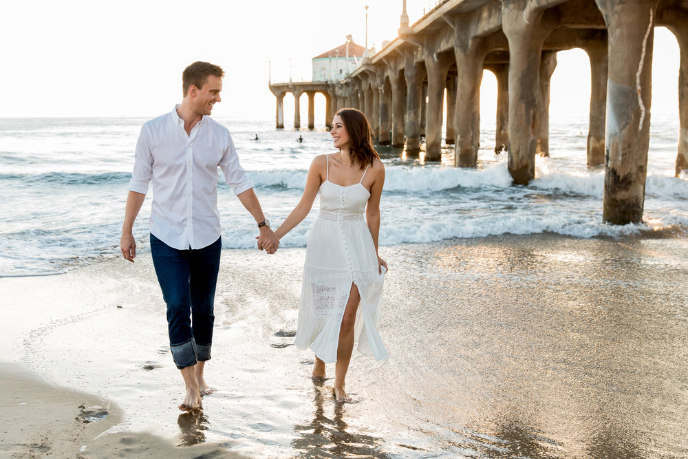  A couple walks on a California beach with the pier behind them 