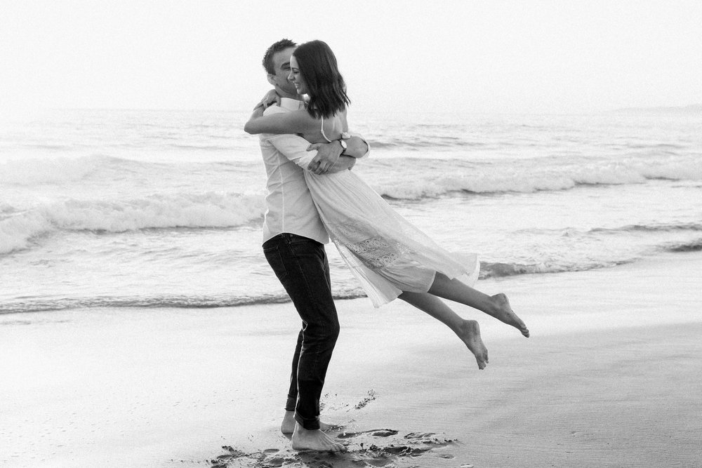  A man swings his bride to be around on the beach 