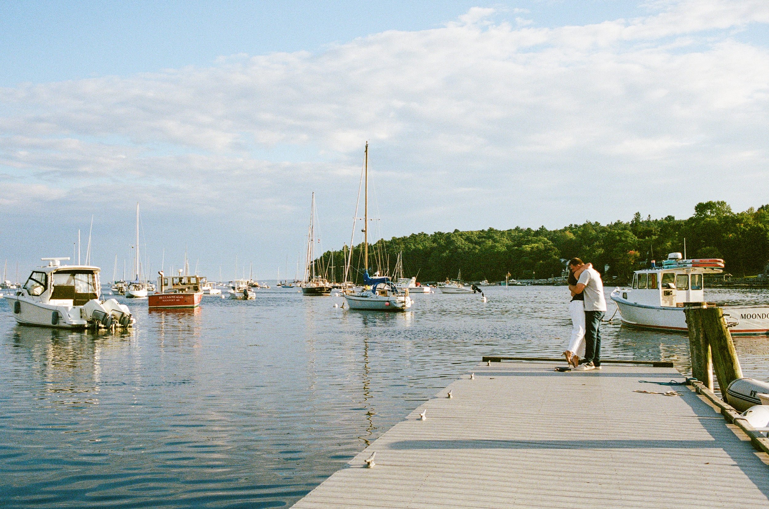 A couple hugs on a dock after being engaged in Rockland, Maine. Photographed on film