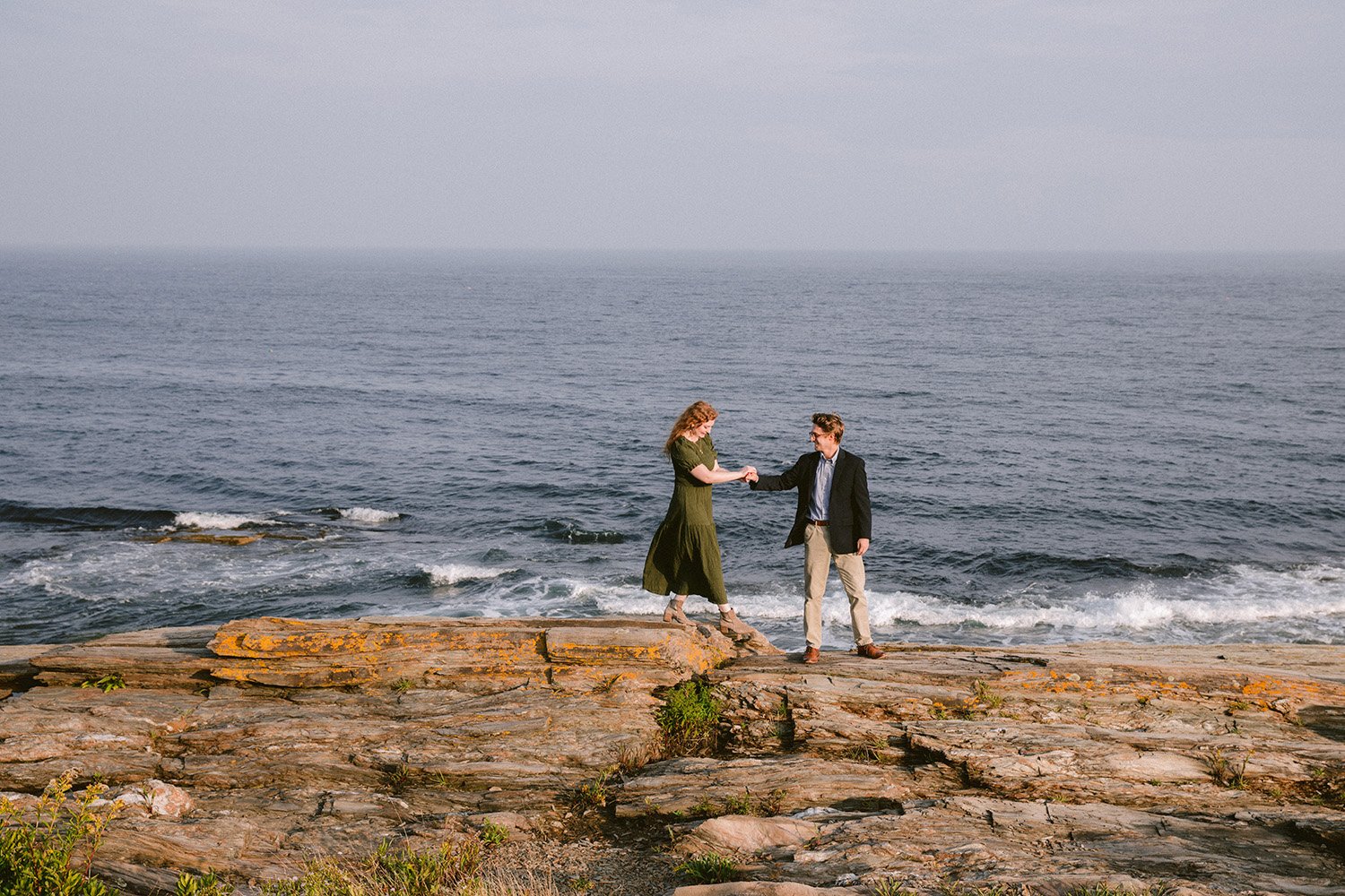 a maine couple walks along the rocks at two lights state park in cape elizabeth