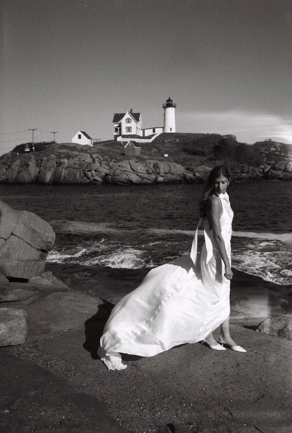 A bride at the Nubble Lighthouse photographed in black and white film with her dress blowing in the wind