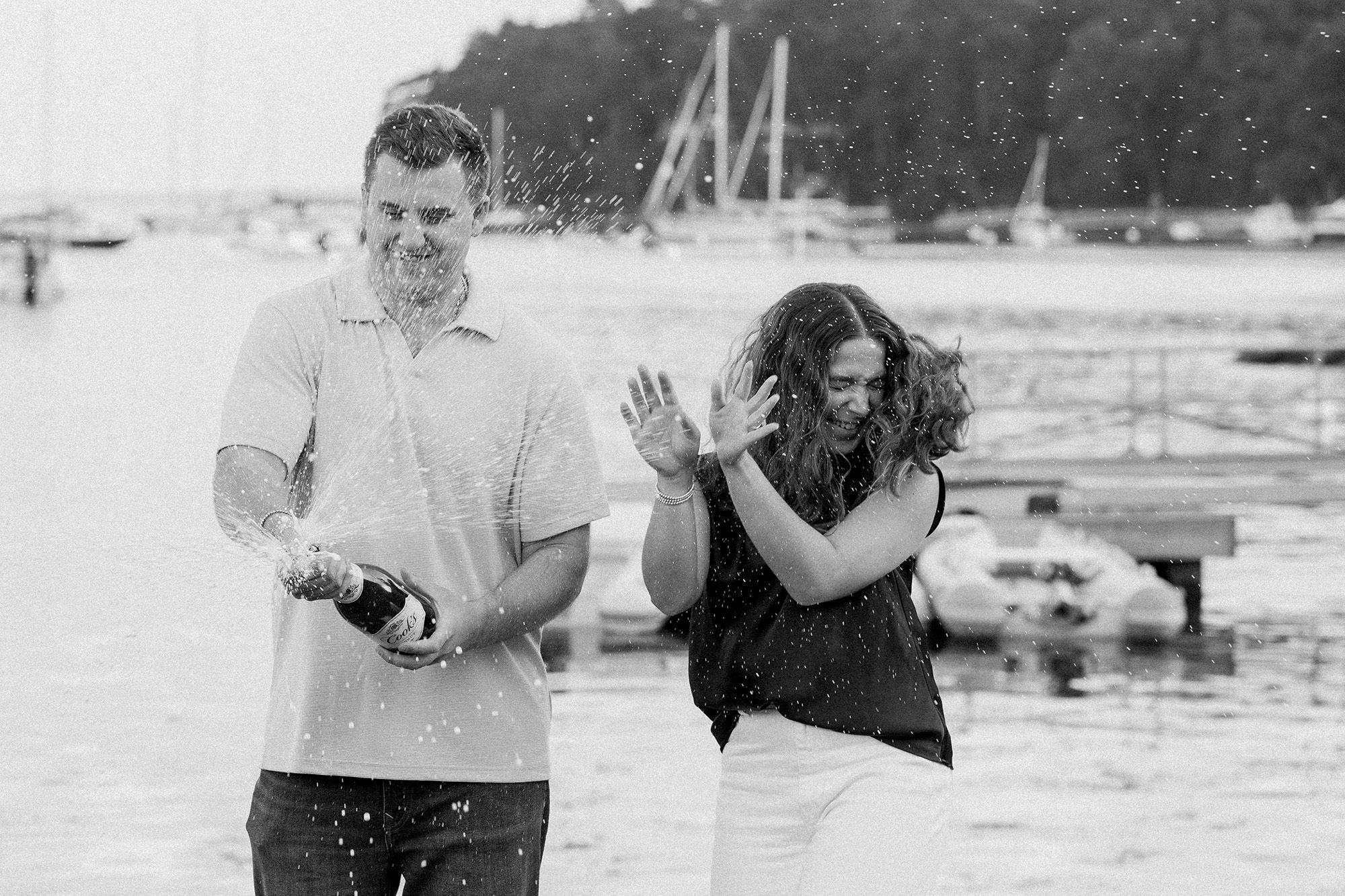 A man pops a bottle of champagne to celebrate an engagement as the woman gets sprayed