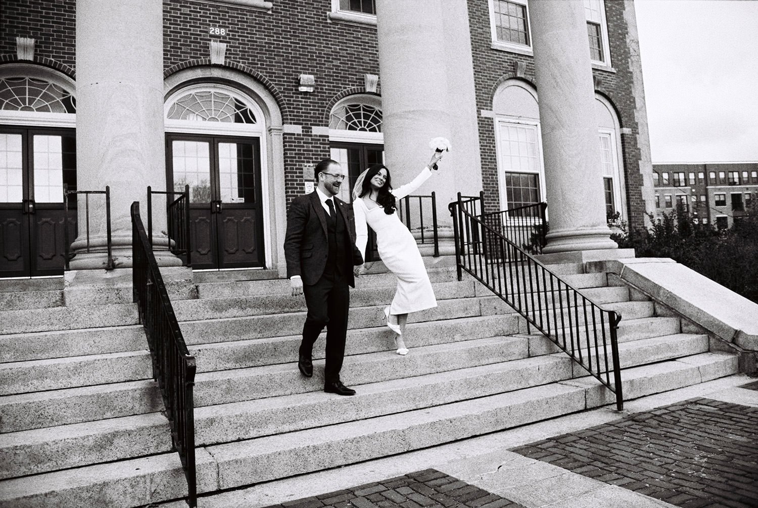 A couple elopes at City Hall and the bride holds up her bouquet, shot with black and white film