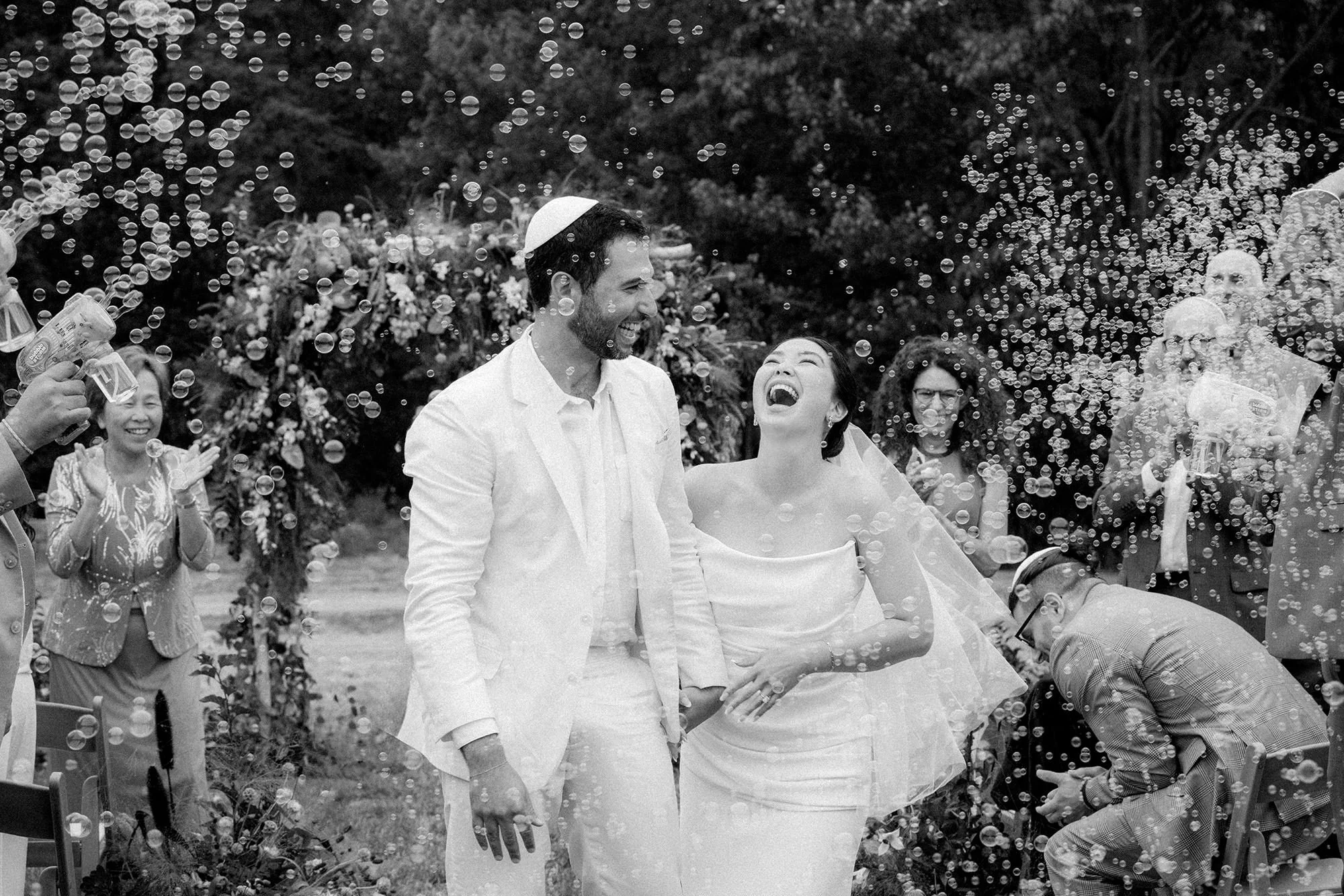 A couple laughs as they walk through bubbles after their ceremony at their Acadia National Park wedding in black and whtie