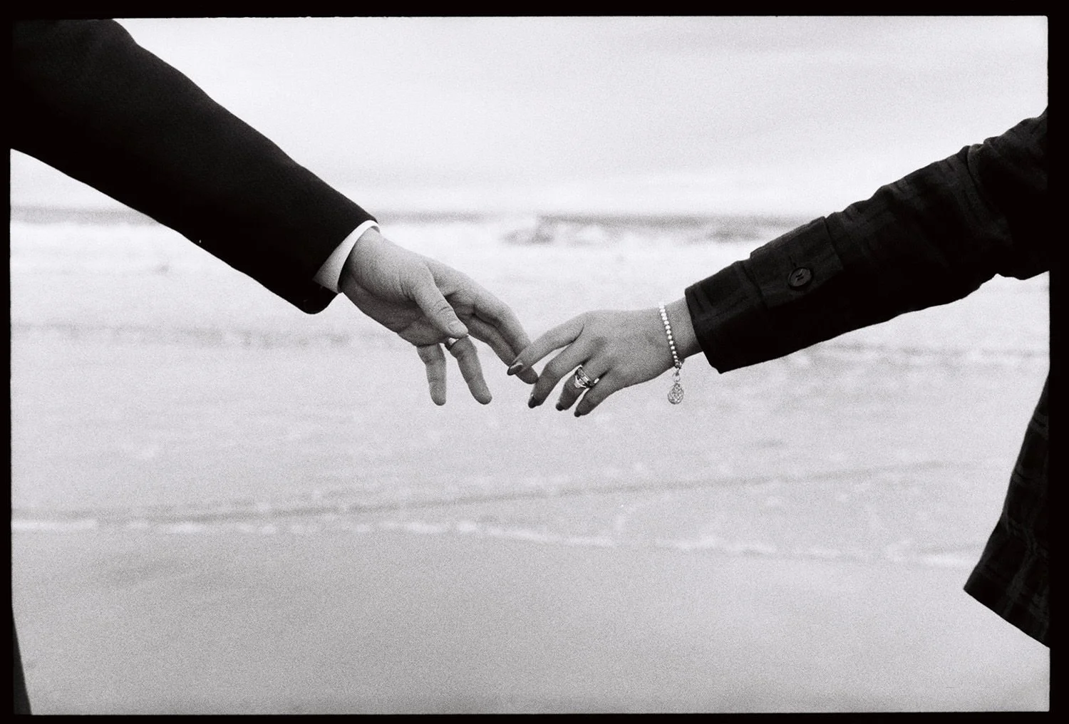 A couple touching fingers by the ocean in black and white film photography