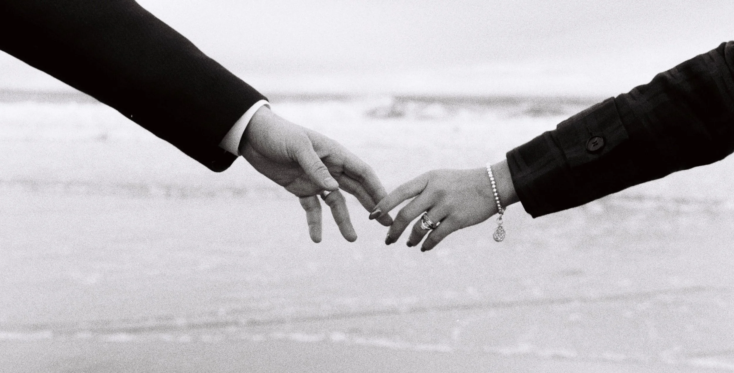 A couple touches fingers in a moody, grainy photo at the beach