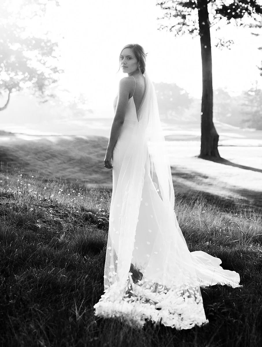A gorgeous bride looks back at the camera in a black and white photograph backlit by the sun