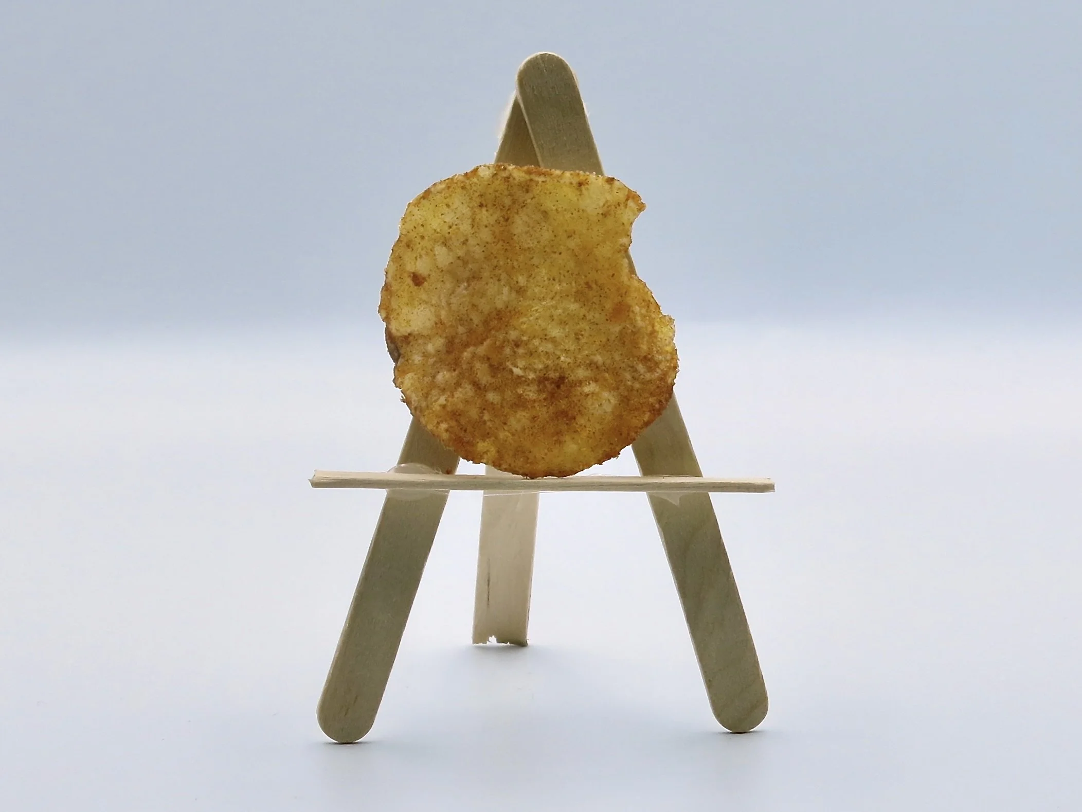 A Miss Vickie's Ketchup potato chip sitting on a popsicle stick easel