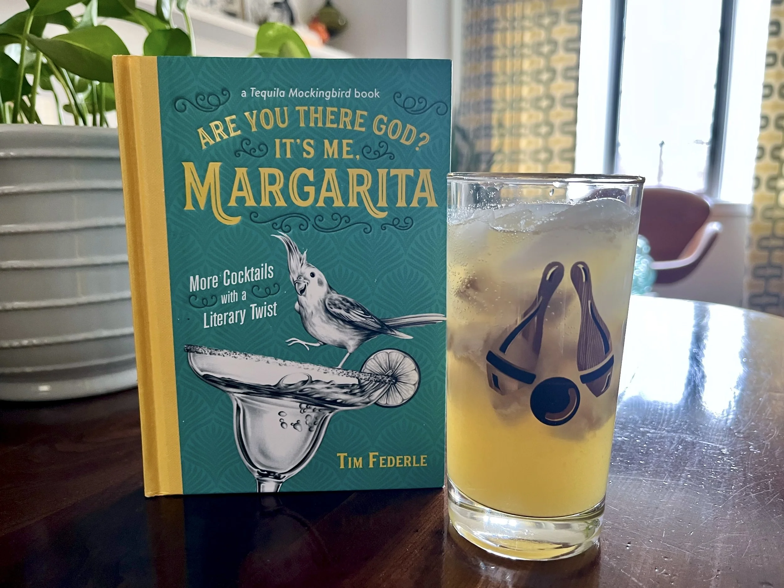 A book titled Are You There God, It's Me Margarita, alongside a glass of containing ginger ale, pineapple juice and frozen banana.