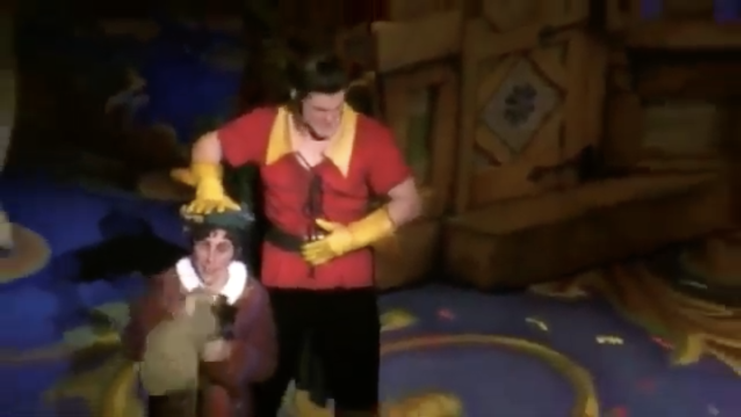 Person wearing a red and yellow costume, possibly a superhero or clown, standing on a colorful stage with a backdrop that resembles a wooden structure.