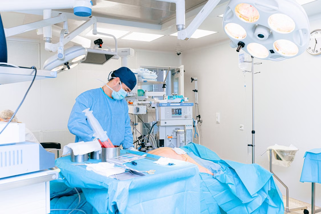 A surgeon in a scrub cap operates on a patient.