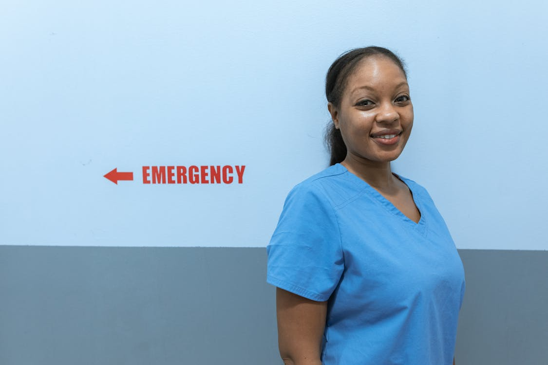 A nurse stands next to the ER sign wearing scrubs.