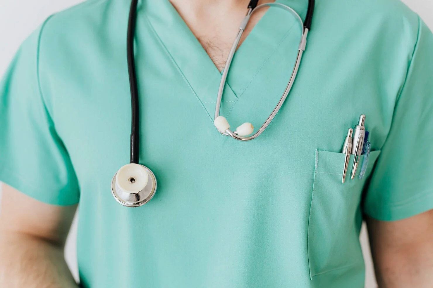 A close-up of a healthcare professional wearing mint-green scrubs, with a stethoscope around the neck and pens in the chest pocket.