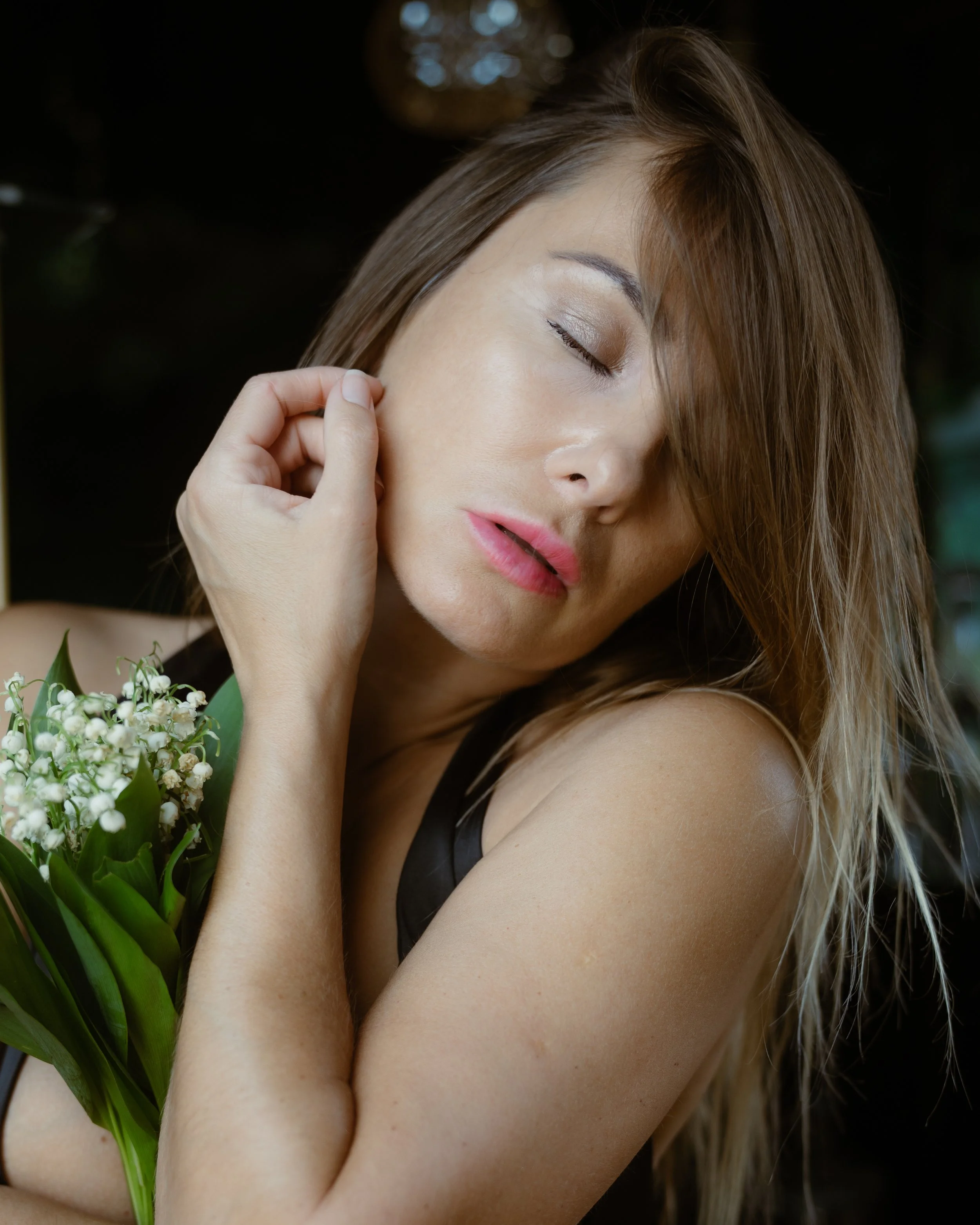 Eine Frau mit braunen Haaren und geschlossenen Augen hält eine Blume an ihr Gesicht.