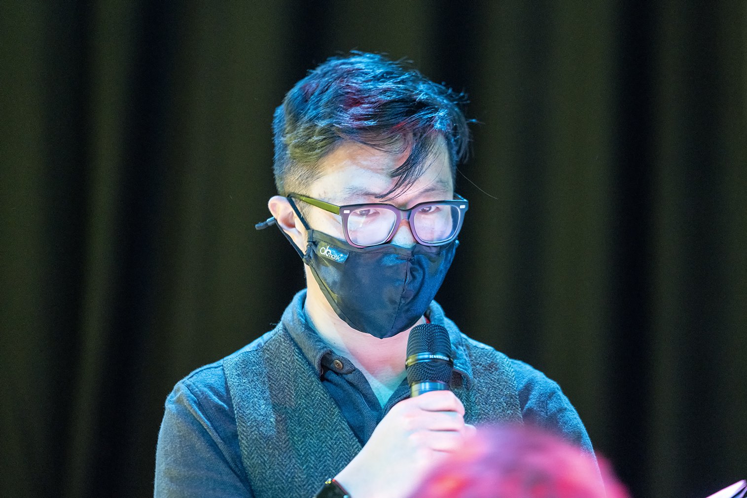 Man wearing glasses and a black mask talking into a mic