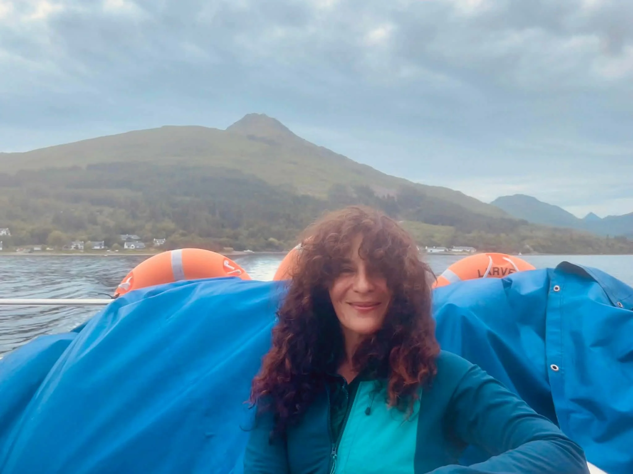 Max on a boat, smiling at the camera, with hills in the background