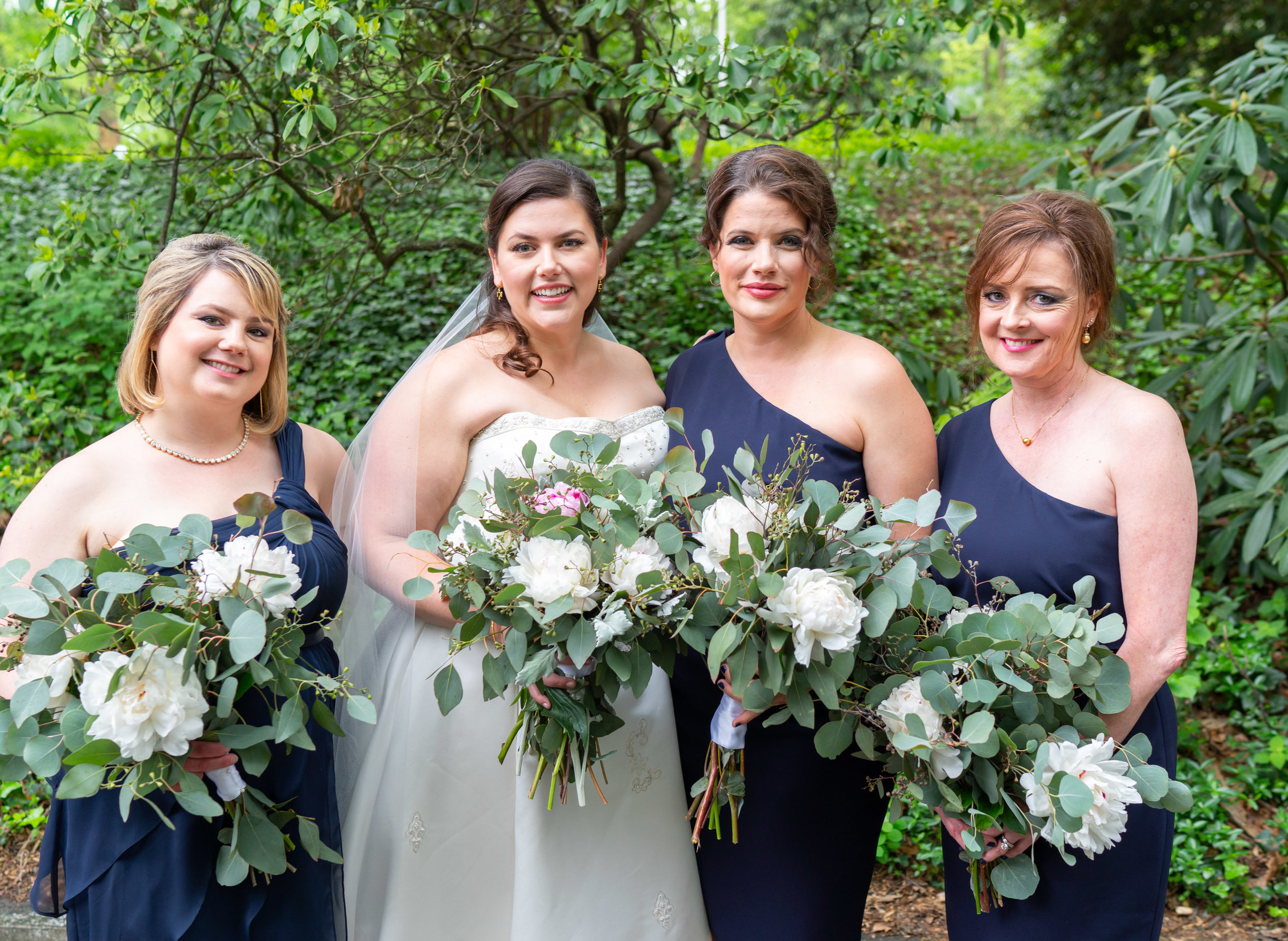 Bride and three bridesmaids in navy dresses and green bouquets at Hendry House