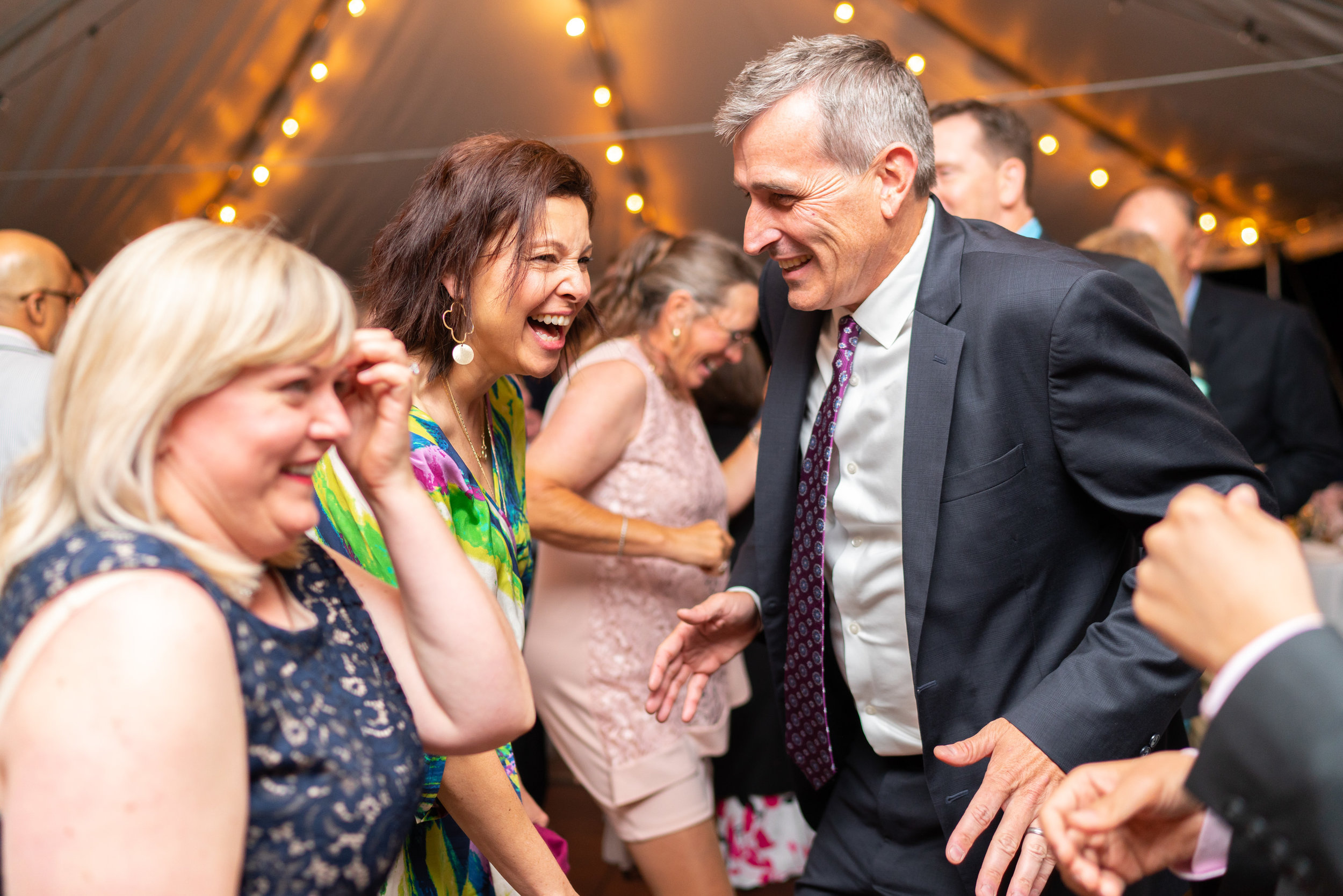 Guests laughing and dancing at Hendry House tented wedding reception with twinkle lights