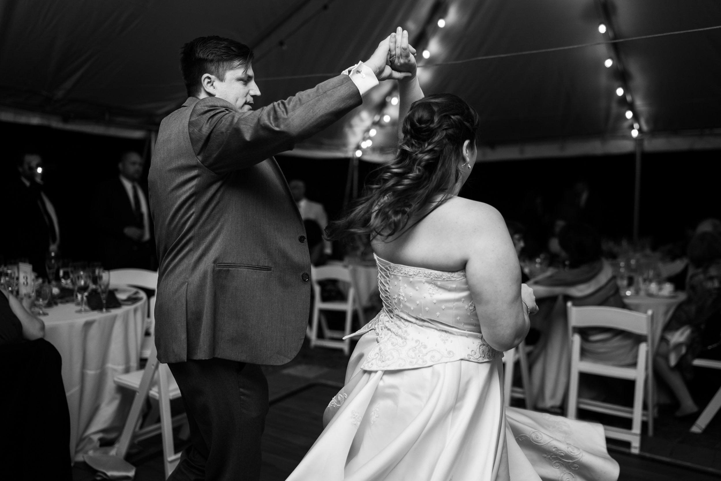 Black and white photo of a groom twirling his bride during the first dance at Hendry House wedding