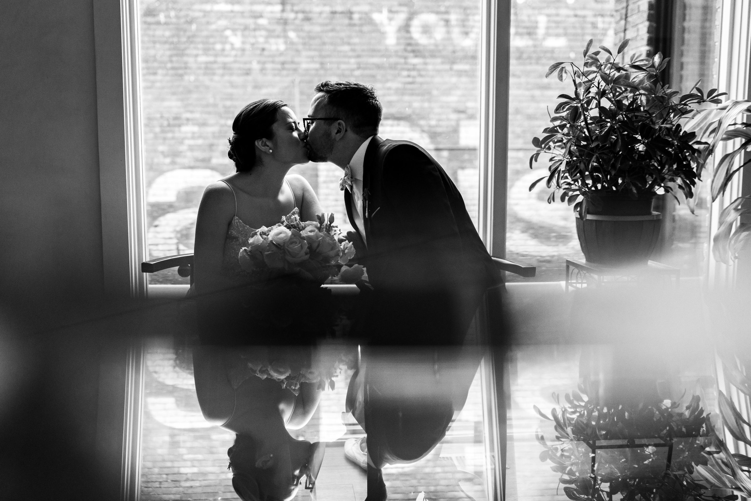 Black and white photo of bride and groom kissing in a window at Gallery OonH