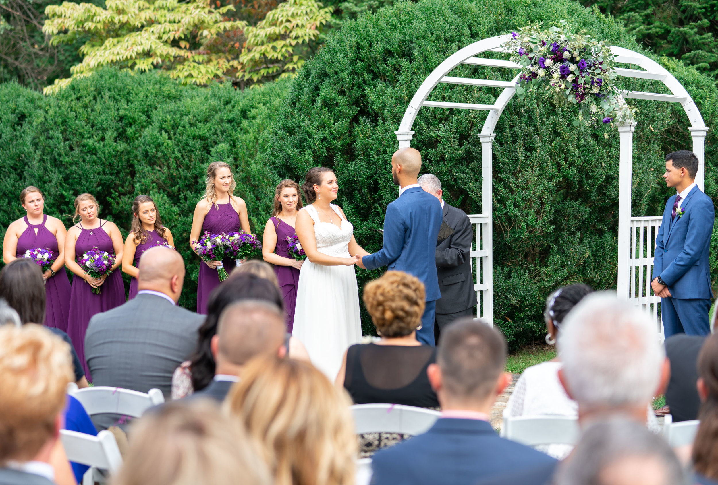 Bride and groom saying their vows under a white arch at Rust Manor House