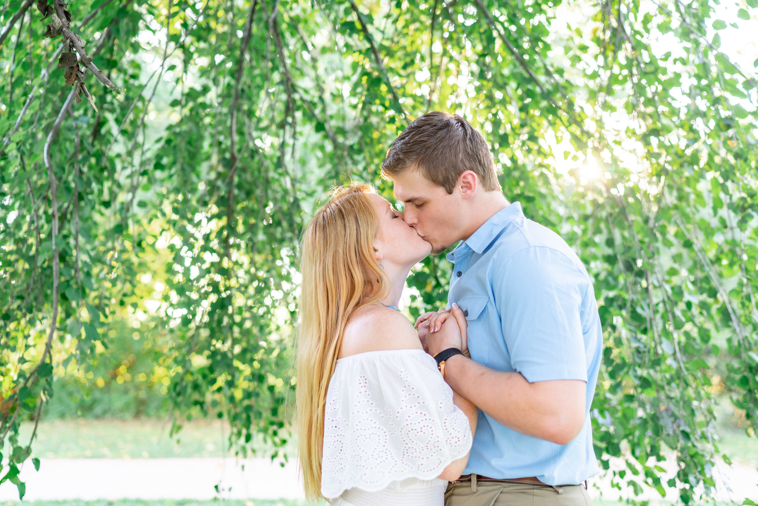 Bride and groom kissing under a willow tree at Baker Park during engagement photos