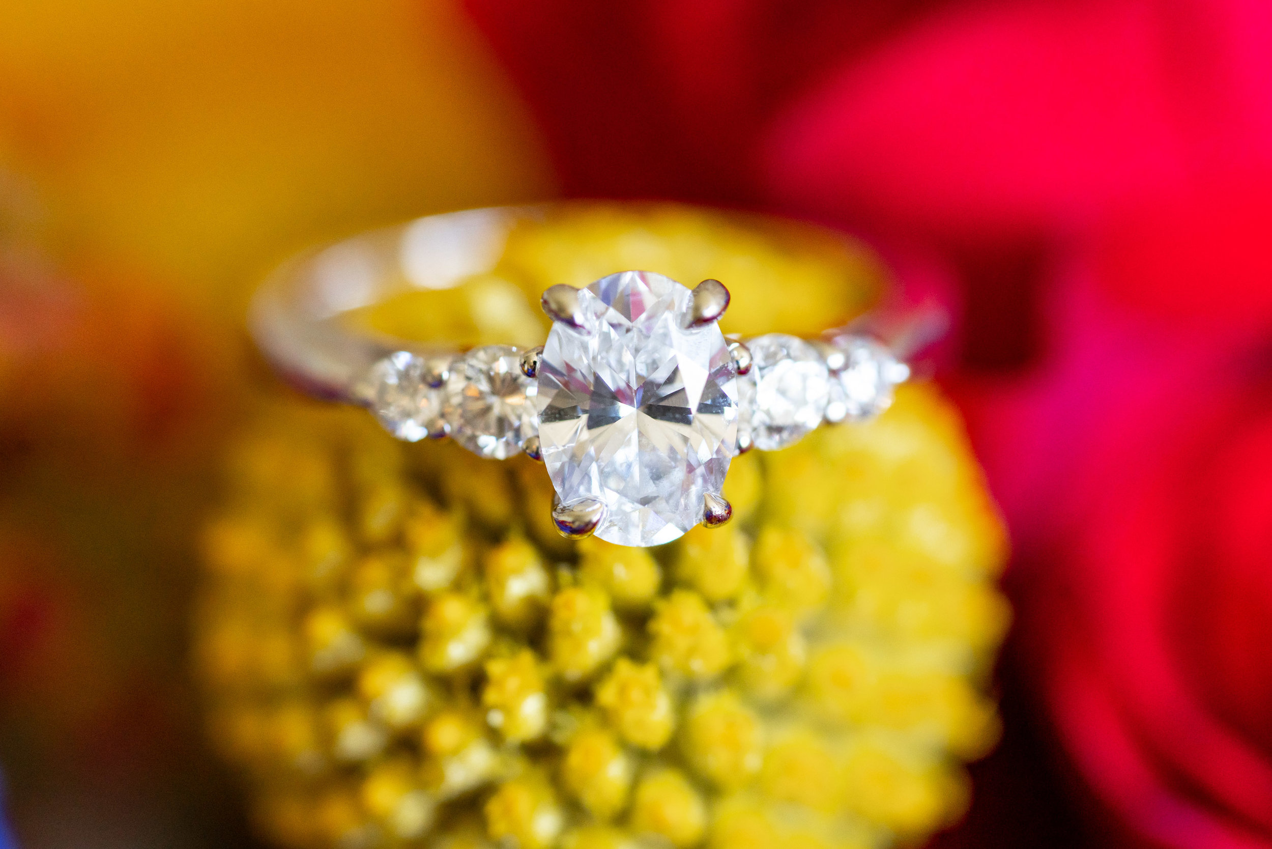 Boone and Son's oval cut three stone engagement ring on yellow craspedia