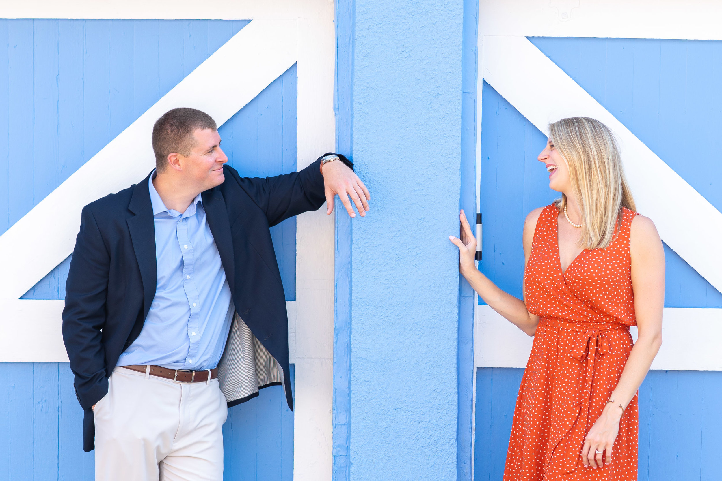 Couple laughing in front of blue wall for engagement photos in annapolis md