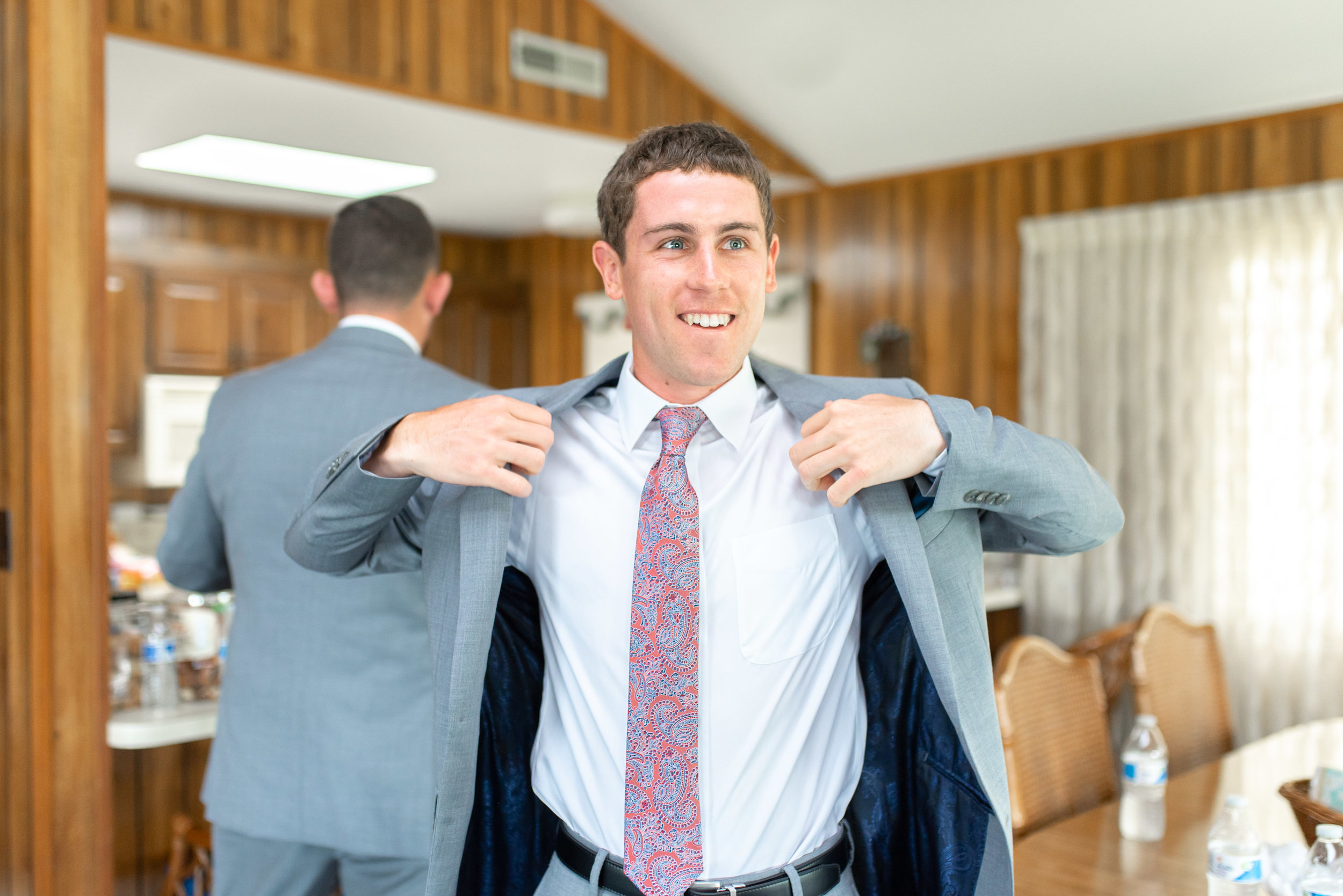 Groom putting on light gray jacket with purple tie for beach wedding