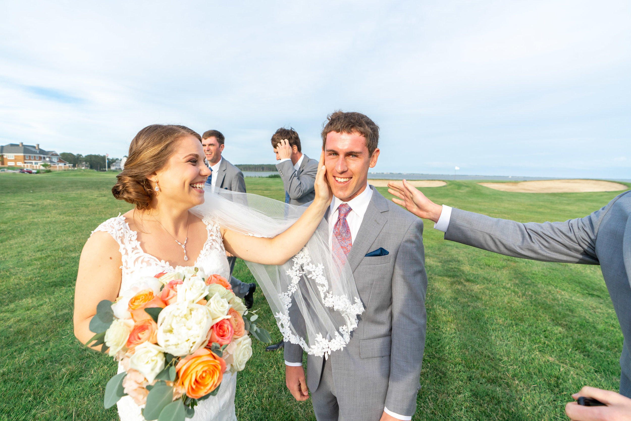 bride with her hand on grooms cheek and ocean in the background