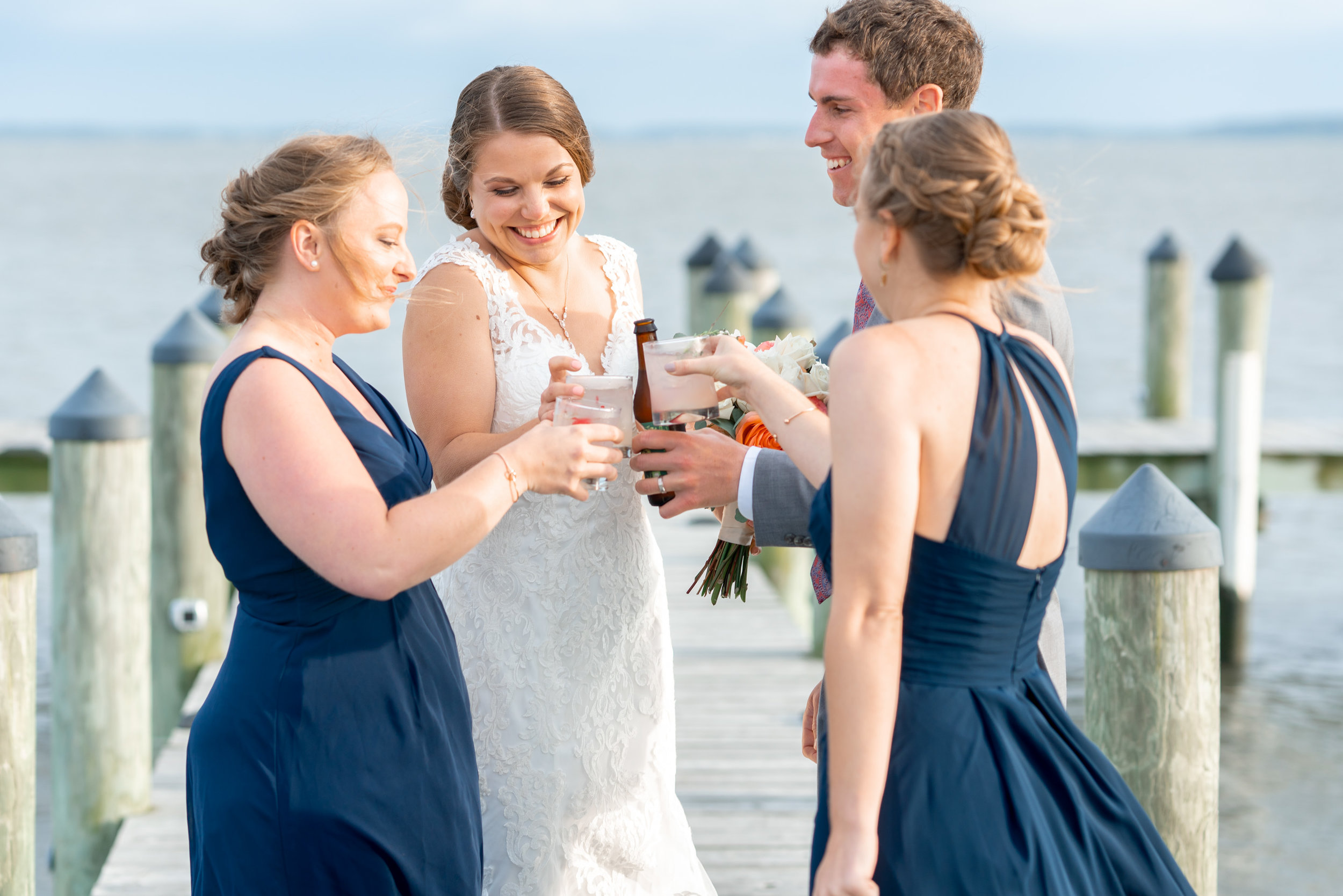 Bridesmaids bring out drinks to the bride and groom on the dock pier